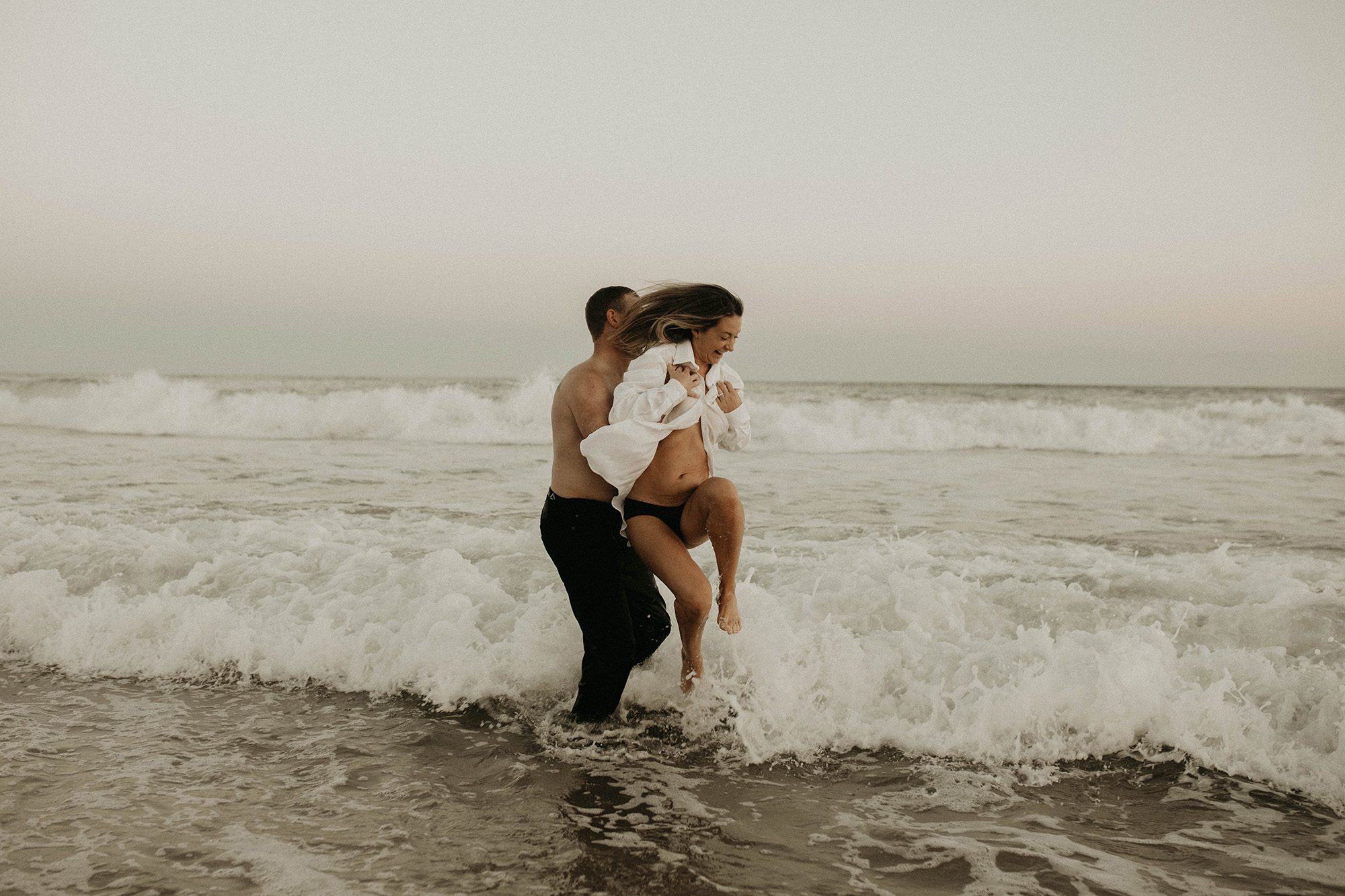 Pregnant couple romantic photoshoot in the waves of the ocean on the shore of the beach. beach maternity portraits