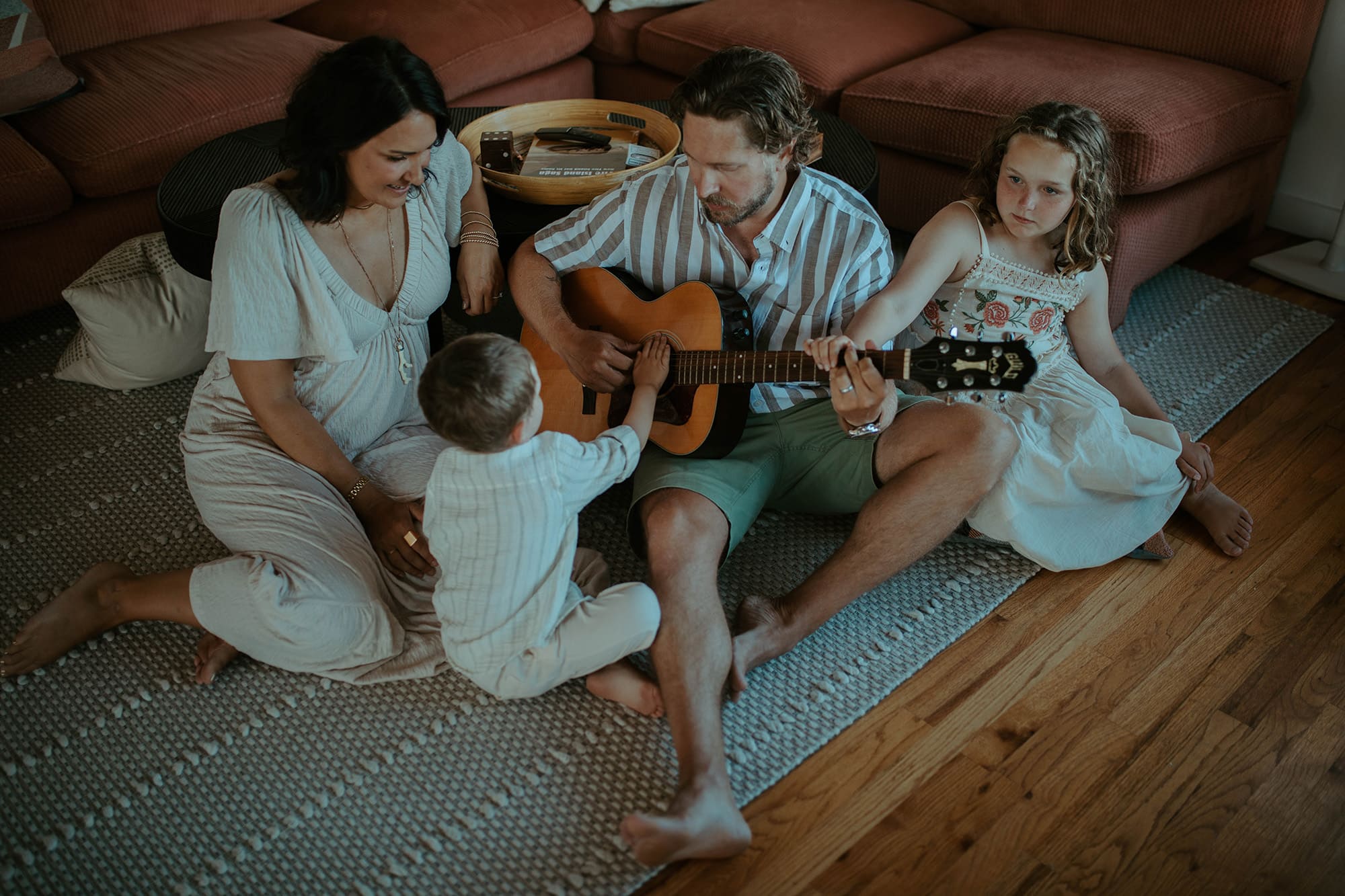 smiling, music loving family sits around a guitar 