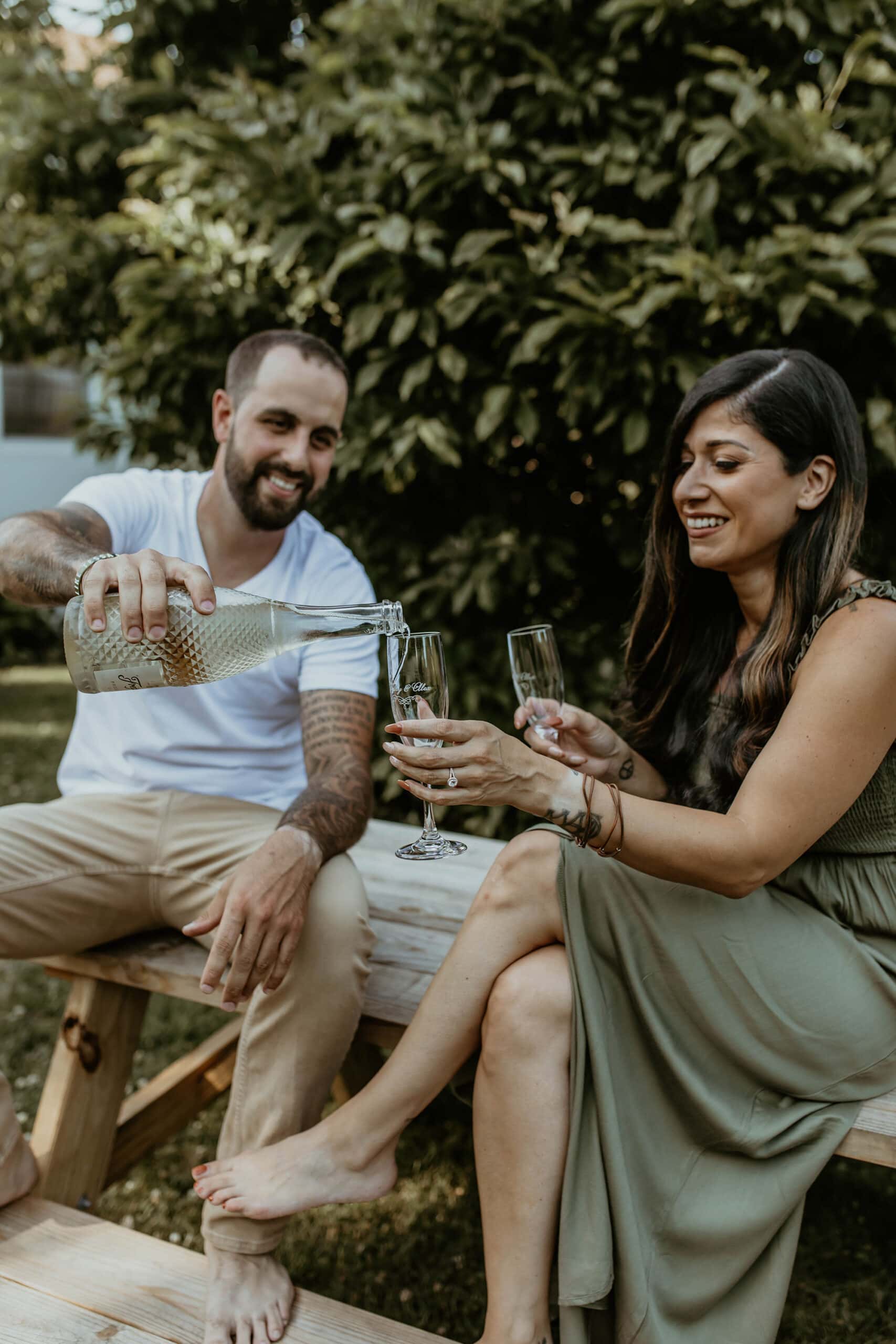 couple sharing wine at a picnic table backyard engagement photoshoot