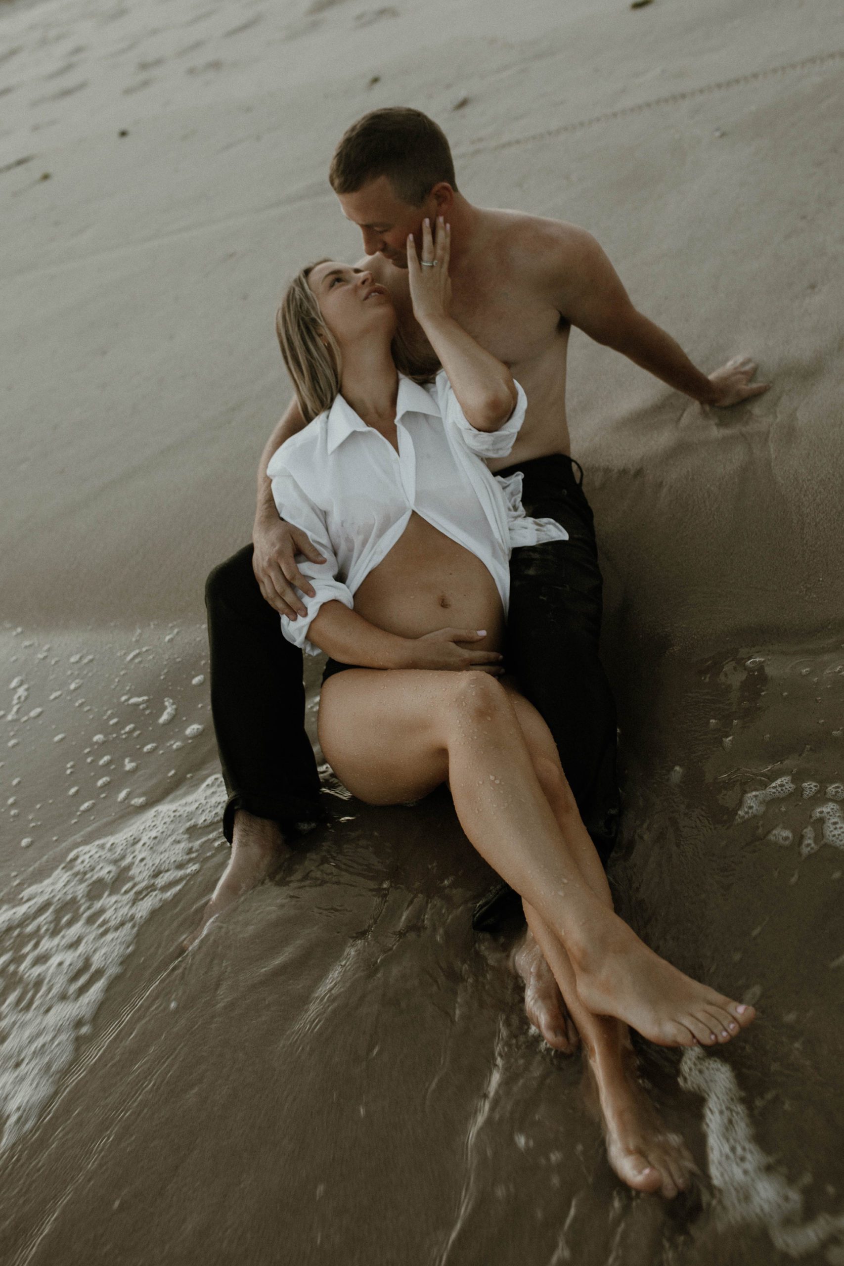 Pregnant couple romantic photoshoot in the waves of the ocean on the shore of the beach. beach maternity portraits