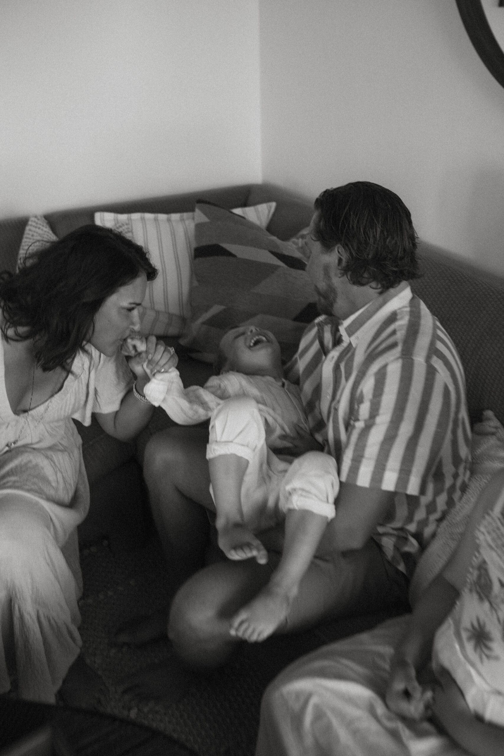 a laughing child held by his mom and dad at a family photoshoot in their beachfront home on fire island in New York 