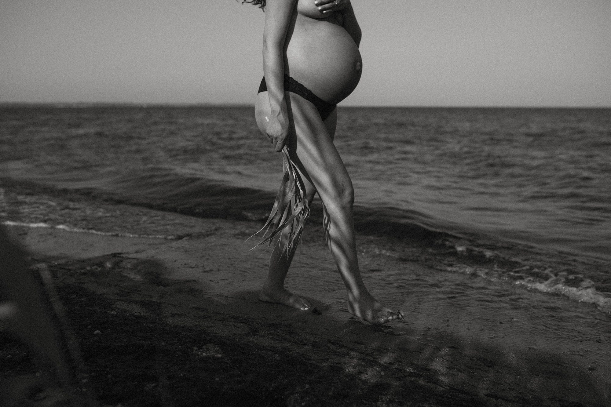 black and white pregnant woman maternity photos walking by the shore of the beach