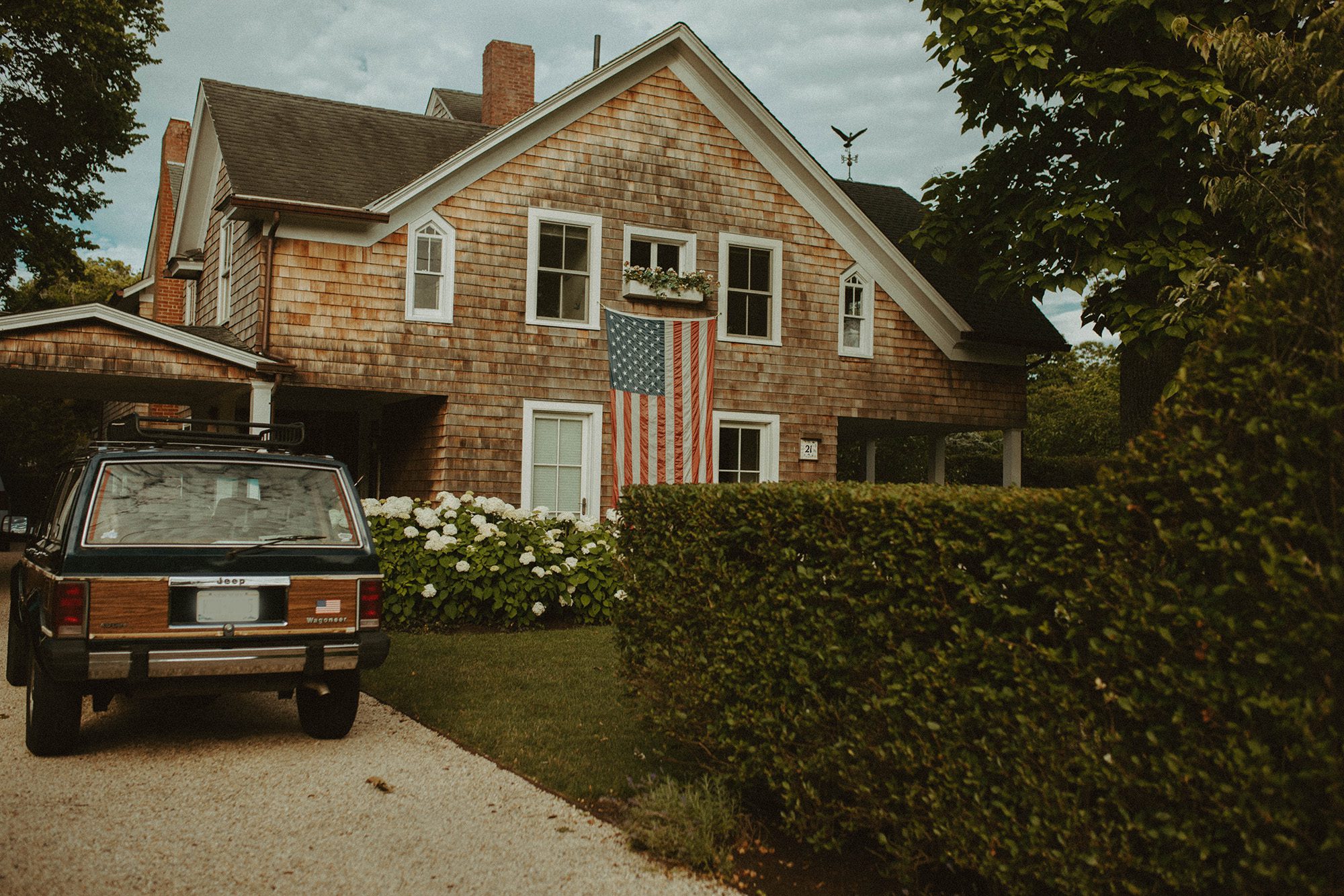 New England style cedar shingle home with American flag and green wood paneled jeep wagoneer