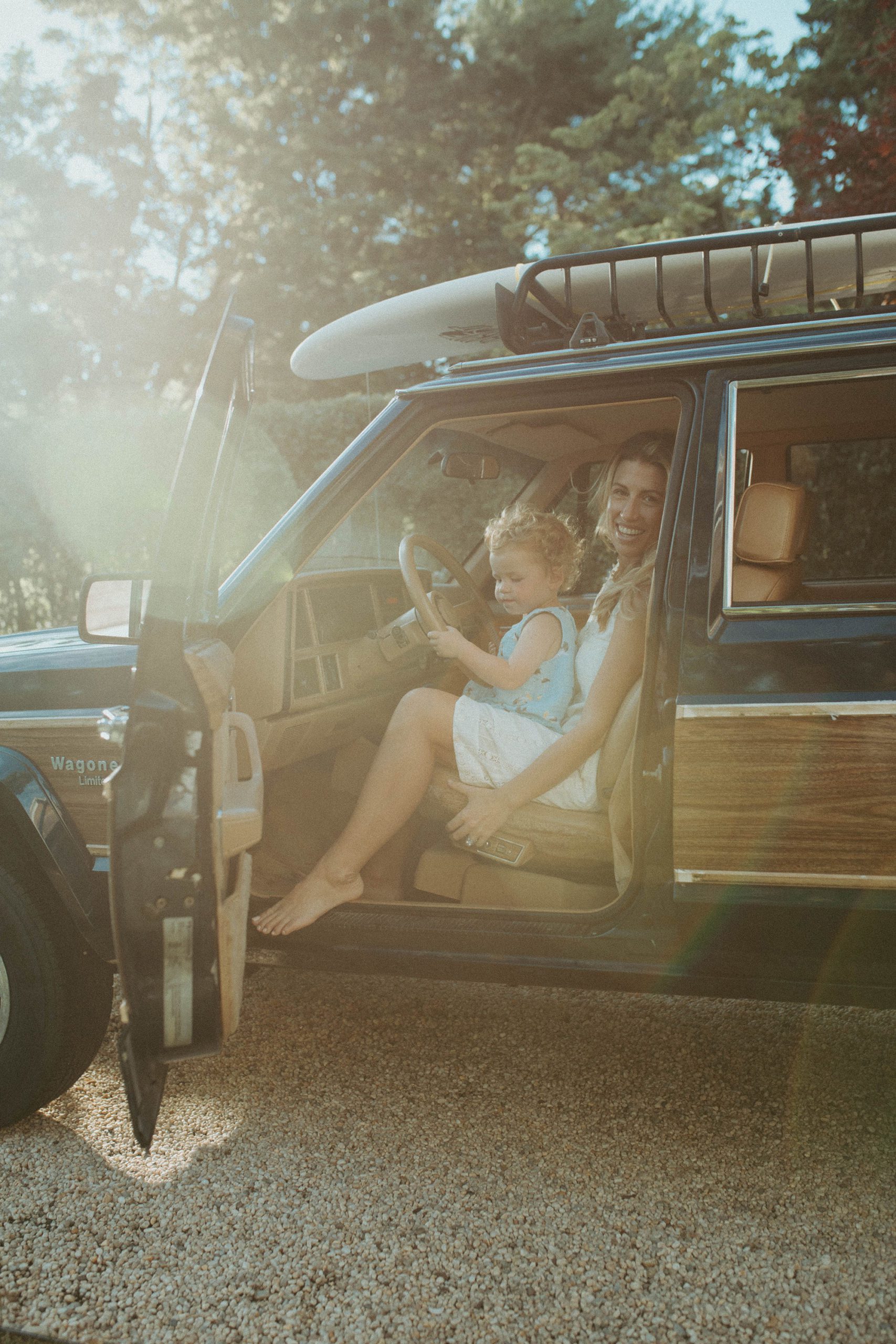 golden hour light, New England mom and baby family photoshoot in the front seat of their wood paneled jeep wagoneer with a surfboard on top in the summertime, Long Island family photographer