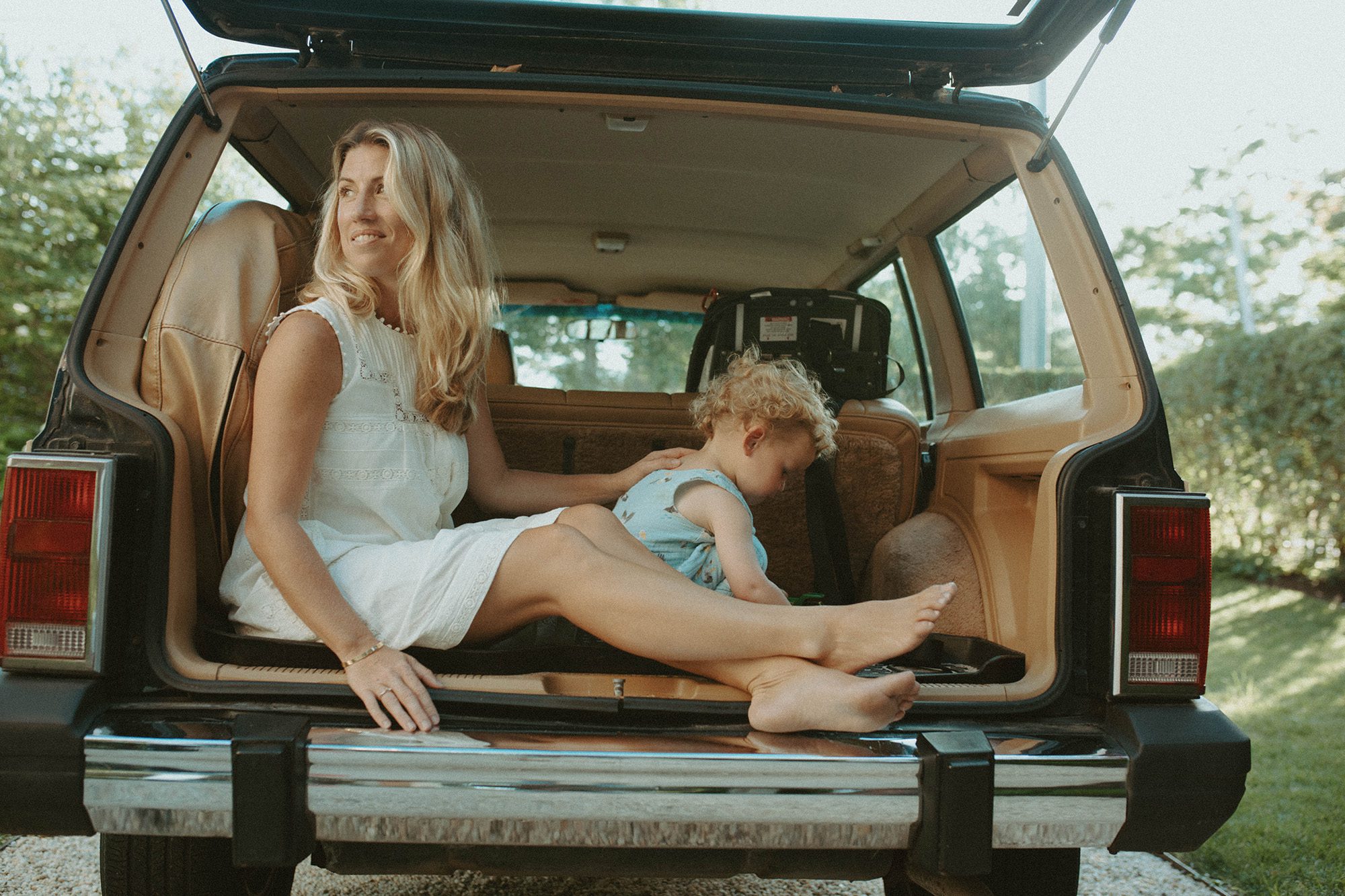 New England mom and baby family portraits in the trunk of their wood paneled jeep wagoneer in the summertime. Long Island family photographer