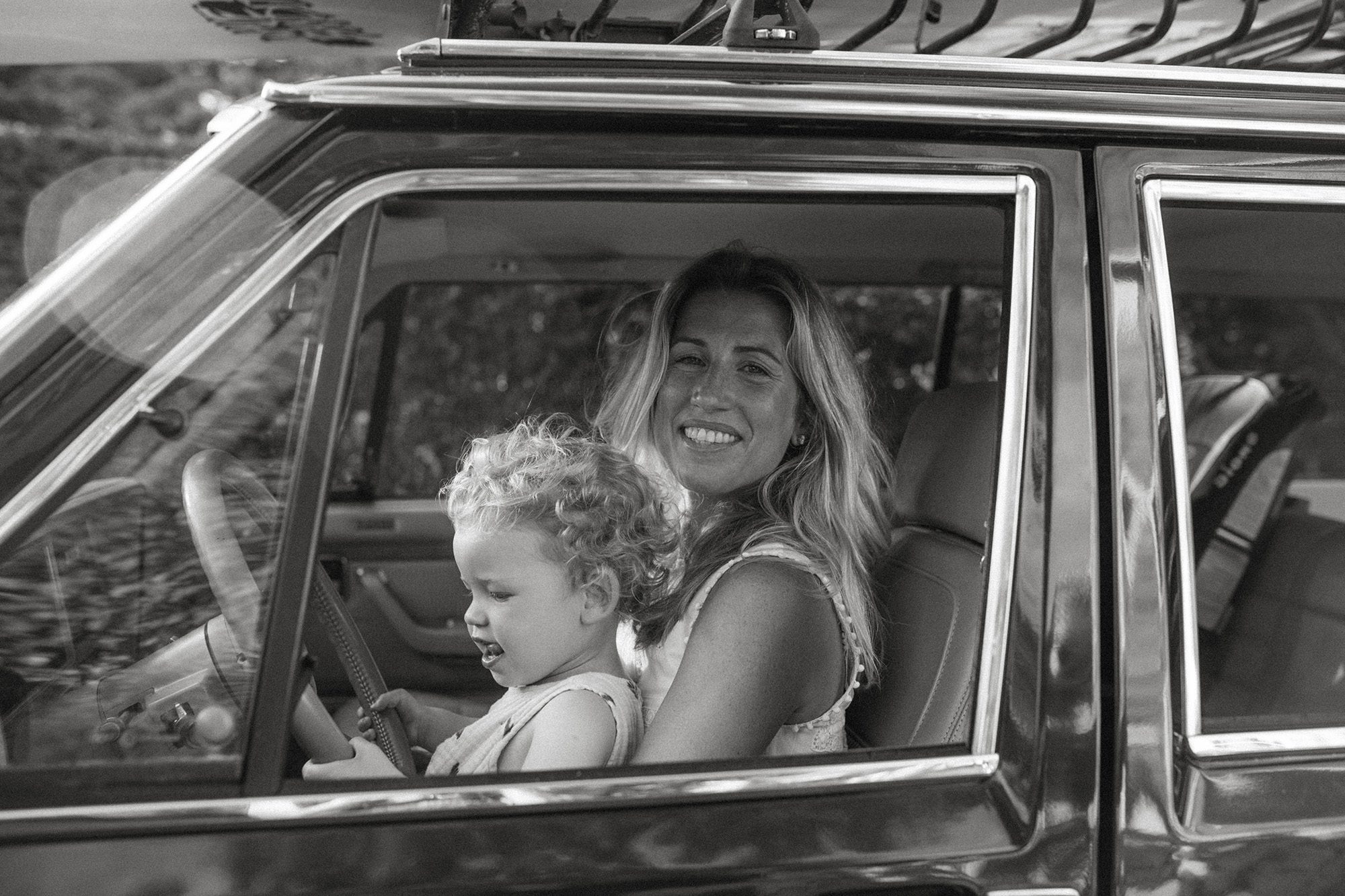 New England mom and baby family portraits in the front seat of their wood paneled jeep wagoneer with a surfboard on top in the summertime