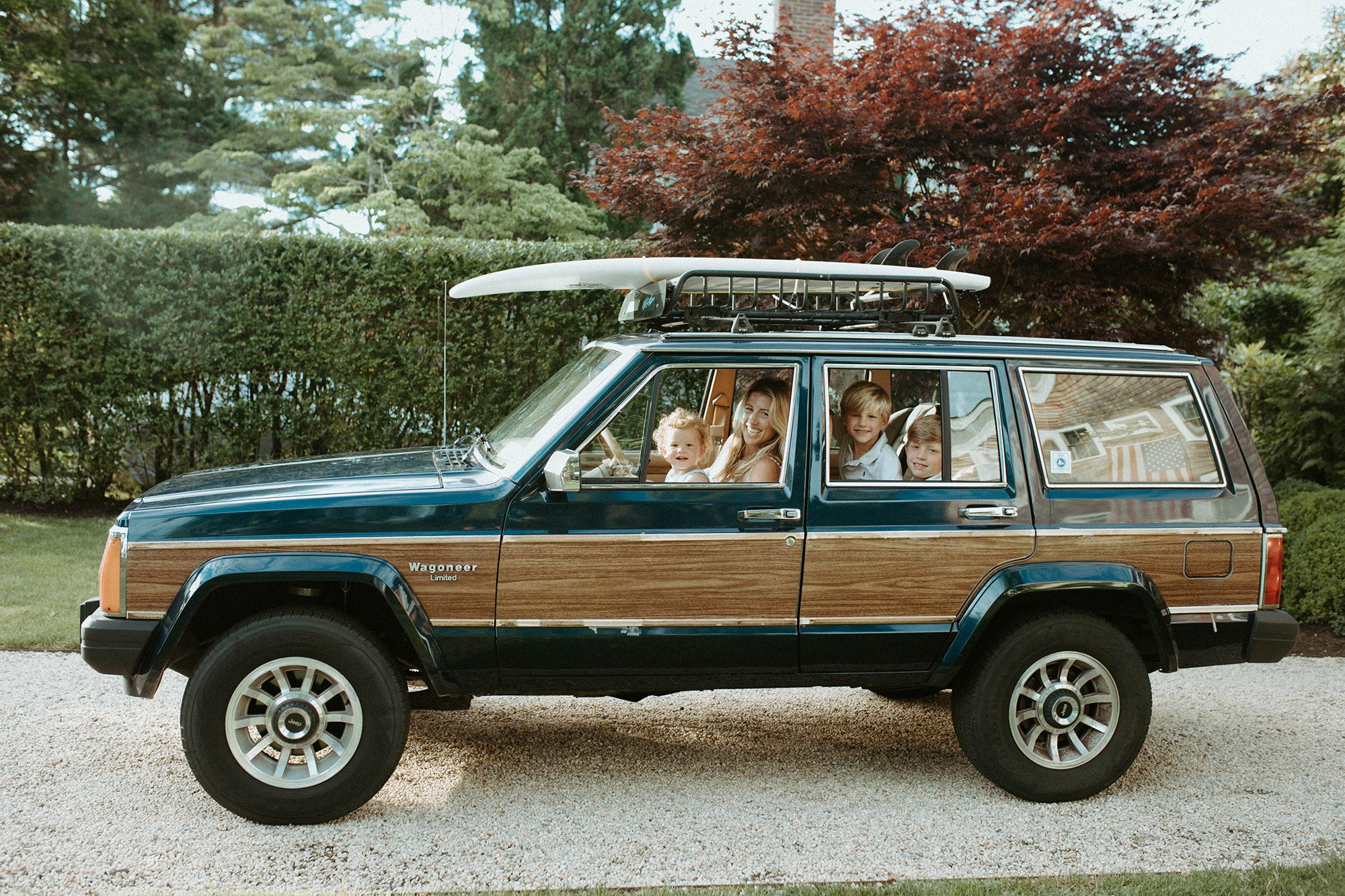 New England mom and son family photos in the front seat of their green wood paneled jeep wagoneer with a surfboard on top in the summertime, Long Island family photographer