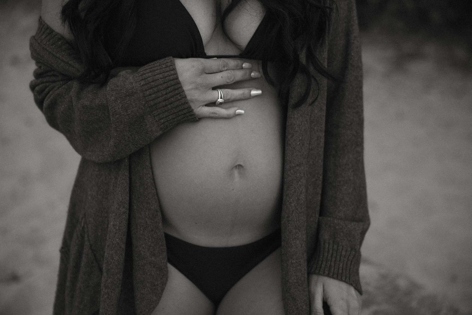 black and white maternity portrait pregnant woman holding belly on the beach